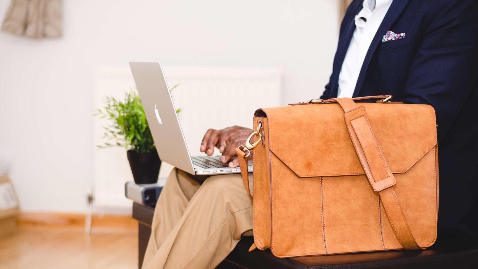 Person Wearing Blue Suit Beside Crossbody Bag and Using Macbook